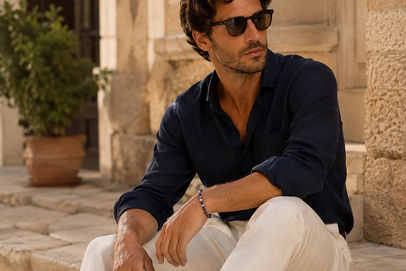 Man wearing a slim blue men’s bracelet with a navy shirt and cream trousers in a Mediterranean setting.