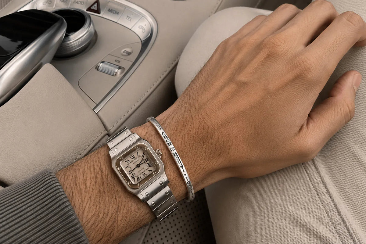 How to Wear Bracelets With a Watch, showing a narrow silver cuff styled next to a square stainless steel watch.