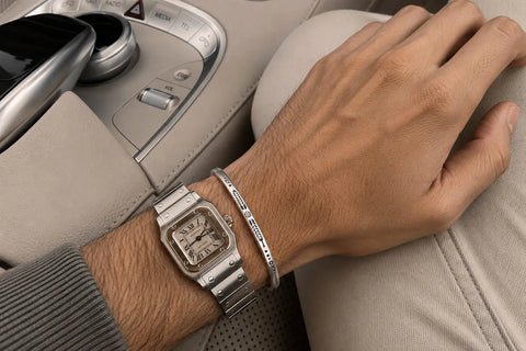 How to Wear Bracelets With a Watch, showing a narrow silver cuff styled next to a square stainless steel watch.