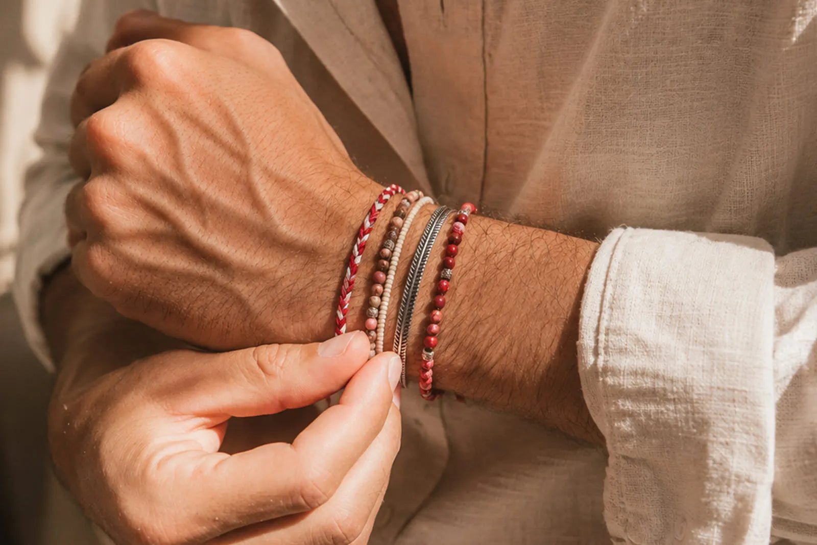 Jasper jewelry for men featuring layered red and neutral stone bracelets styled with a beige linen shirt.