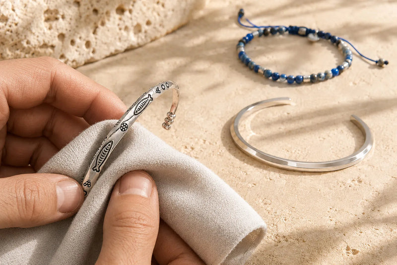 Jewelry tarnish being removed from a silver bracelet with a soft polishing cloth beside men’s bracelets.