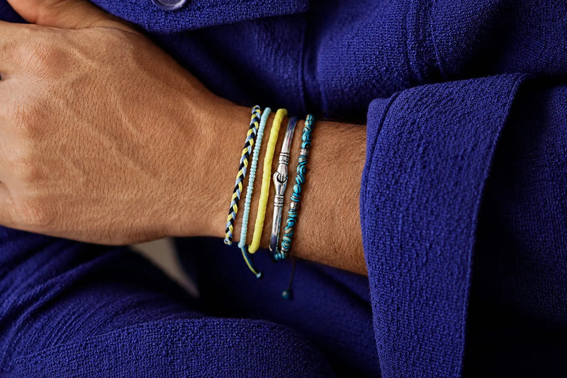 Match Bracelet Colors With Outfits using blue, yellow, turquoise, and silver bracelets styled with a deep blue men’s outfit.