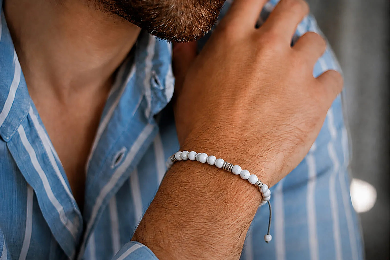 Men wearing a white beaded bracelet with a light blue striped shirt for a relaxed summer outfit.