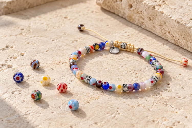 Multicolored glass beads on adjustable cord beside loose patterned beads on pale stone.