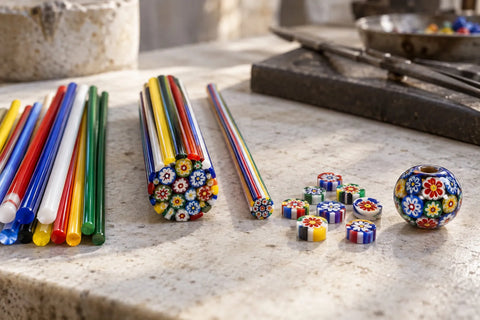 Bead Colorful millefiori glass canes, patterned slices and a finished bead arranged on a pale stone work surface.