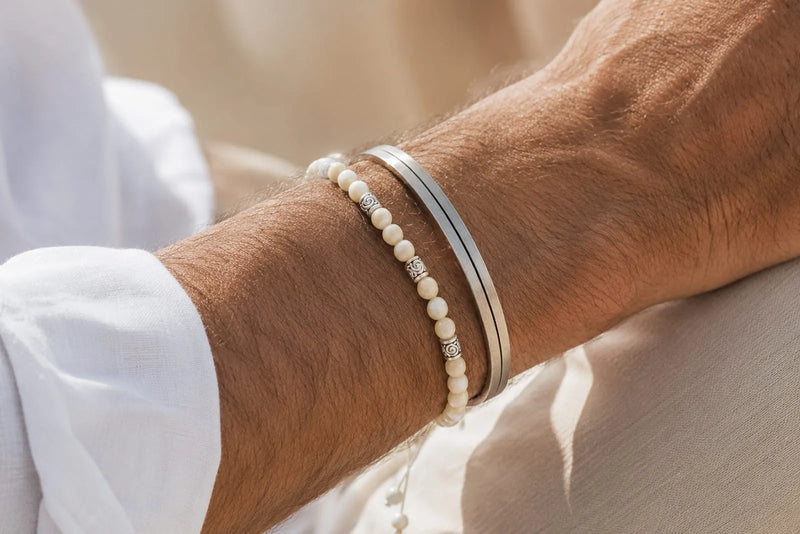 Mother of pearl and silver bracelet worn together on a man’s wrist in warm natural light.
