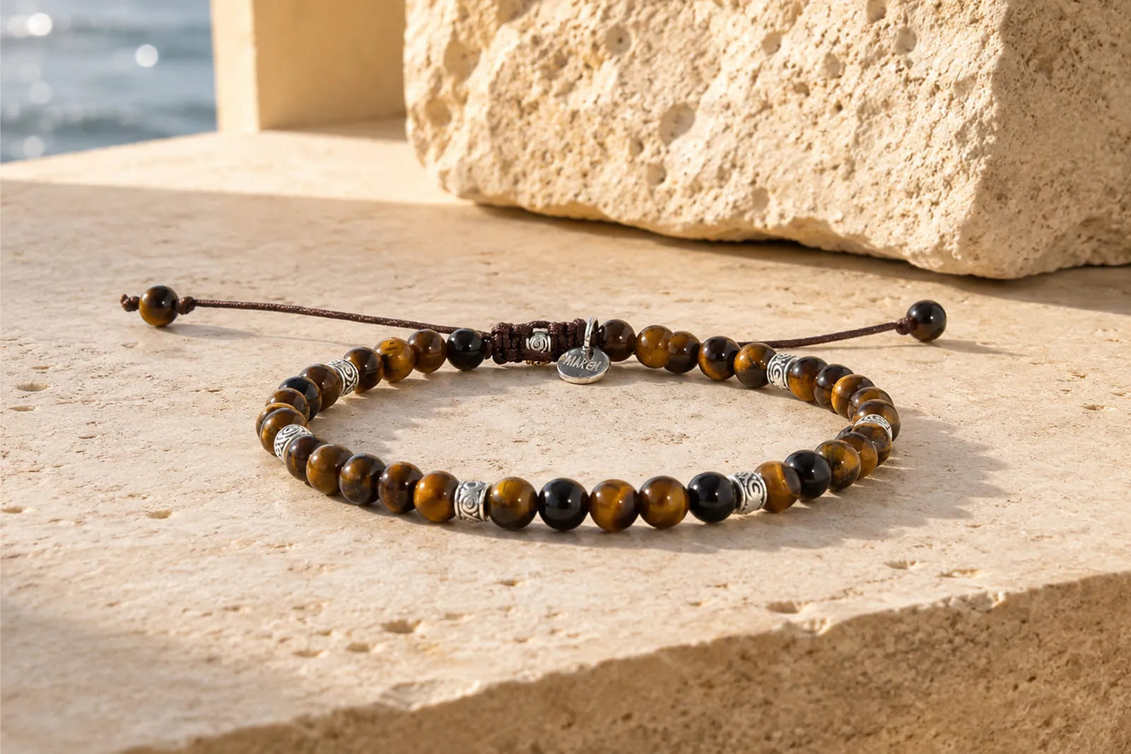 Real Tiger Eye bracelet with brown and golden chatoyant beads resting on warm Mediterranean stone in natural sunlight.