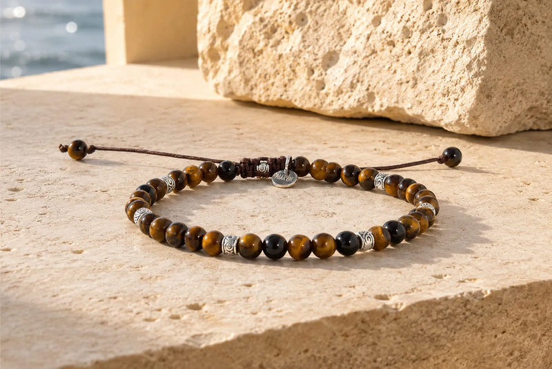 Real Tiger Eye bracelet with brown and golden chatoyant beads resting on warm Mediterranean stone in natural sunlight.