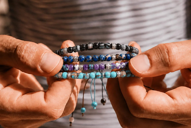 Real vs Fake Jasper comparison featuring black, blue, purple, and turquoise beaded bracelets held between two hands.