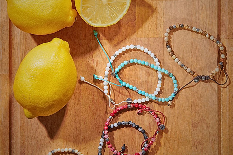 Colorful stone bracelet styles arranged on a wooden surface beside fresh lemons.