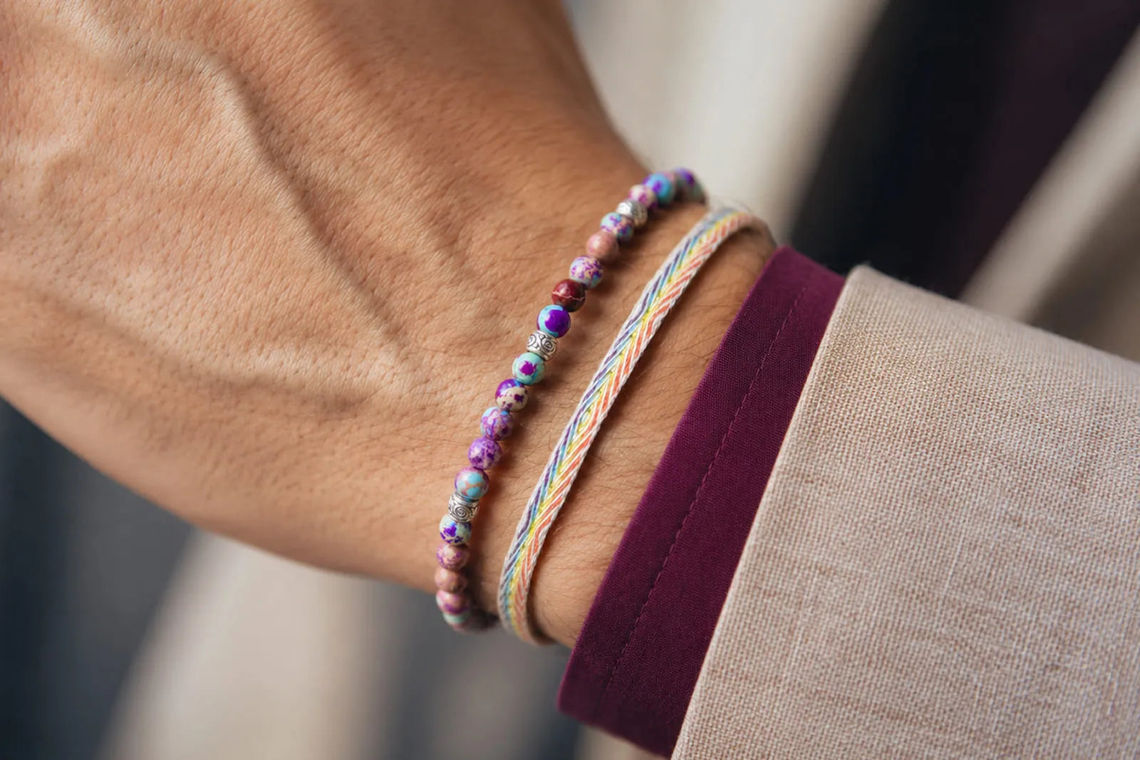 Sea Sediment Jasper bracelet with small multicolored beads styled beside a woven cord bracelet and beige suit sleeve.