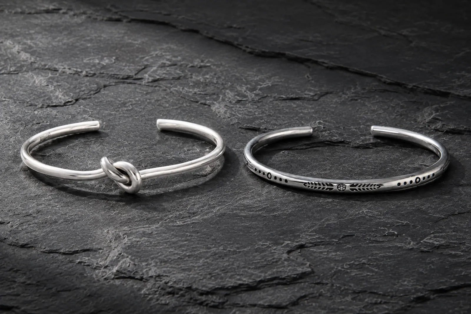 Sterling silver or stainless steel men’s cuff bracelets displayed side by side on dark stone