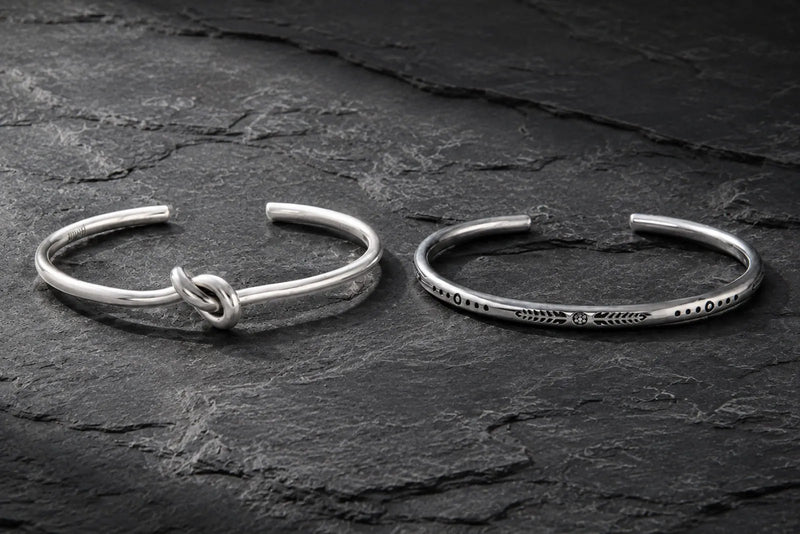 Sterling silver or stainless steel men’s cuff bracelets displayed side by side on dark stone