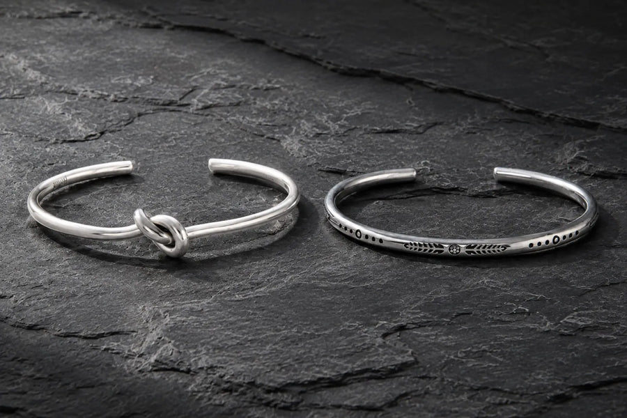 Sterling silver or stainless steel men’s cuff bracelets displayed side by side on dark stone