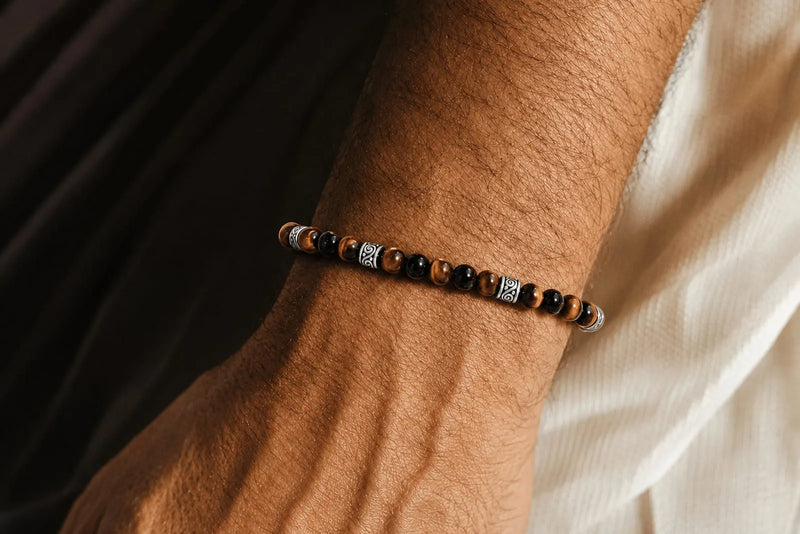 Tiger’s eye meaning featured in a slim men’s bracelet with polished brown beads and silver details.