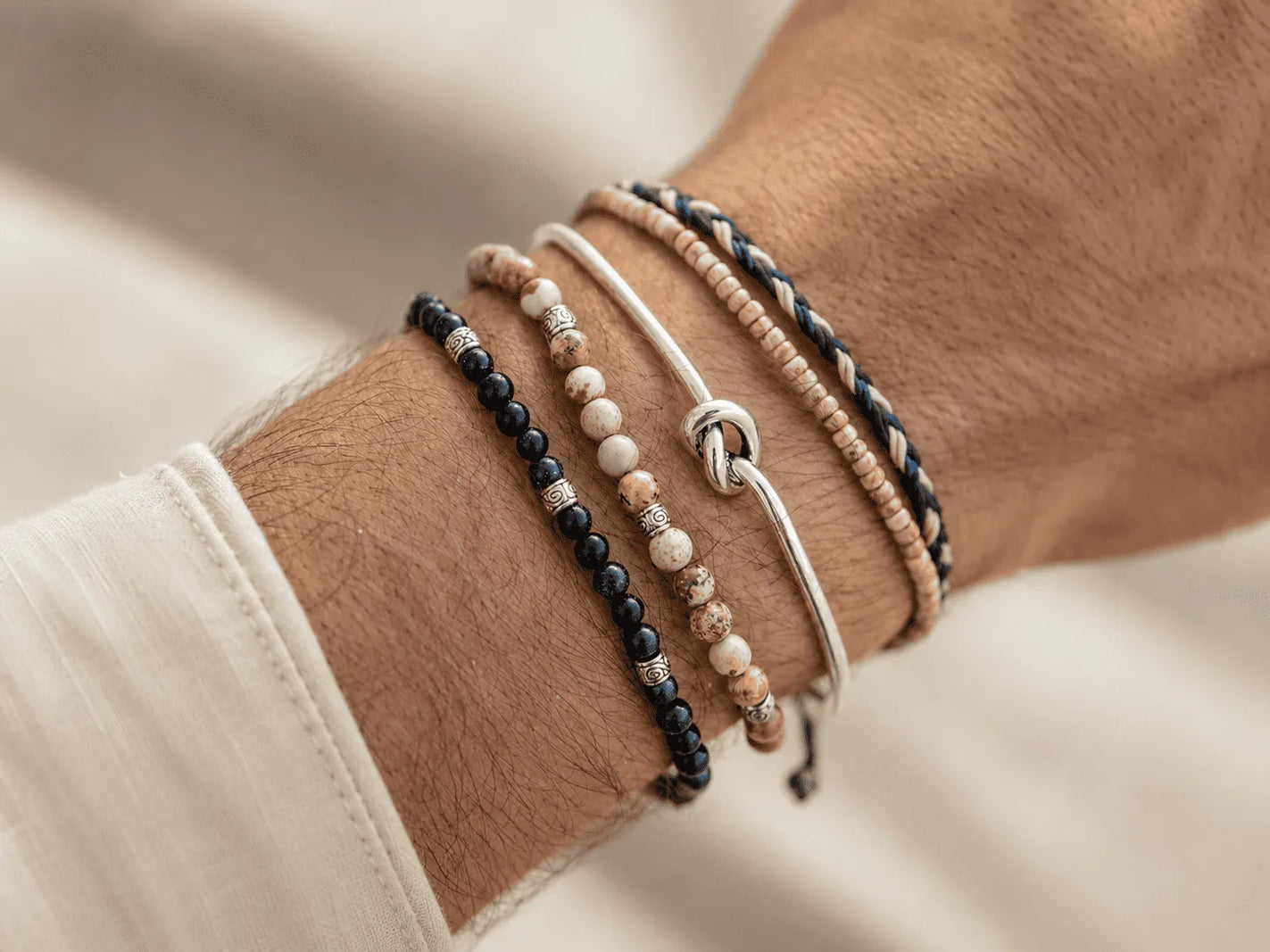 Man wearing stacked stone bead, seed bead, woven, and silver bangle bracelets.