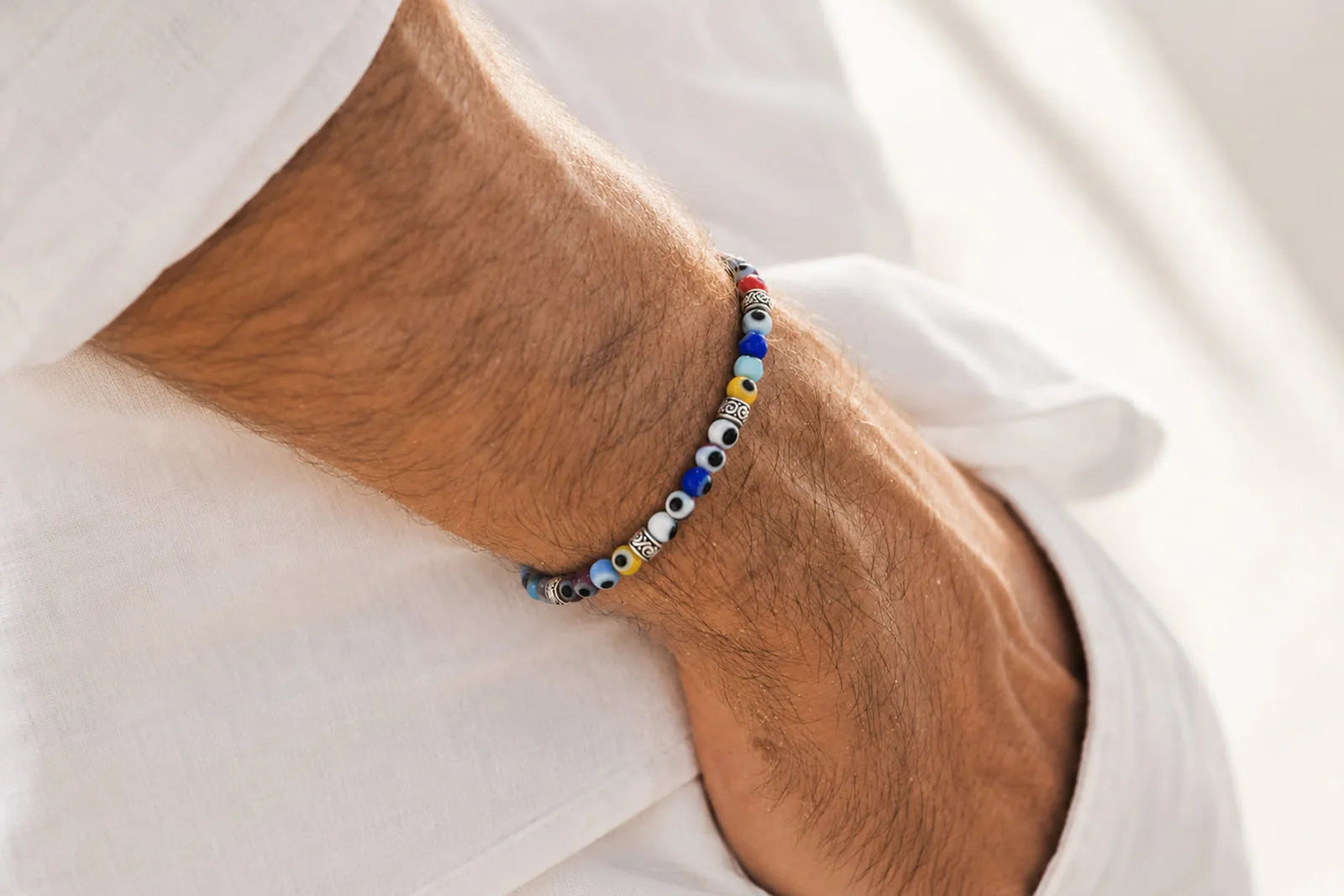 What is an evil eye bracelet, a colorful beaded bracelet with traditional eye motifs worn on a man’s wrist.