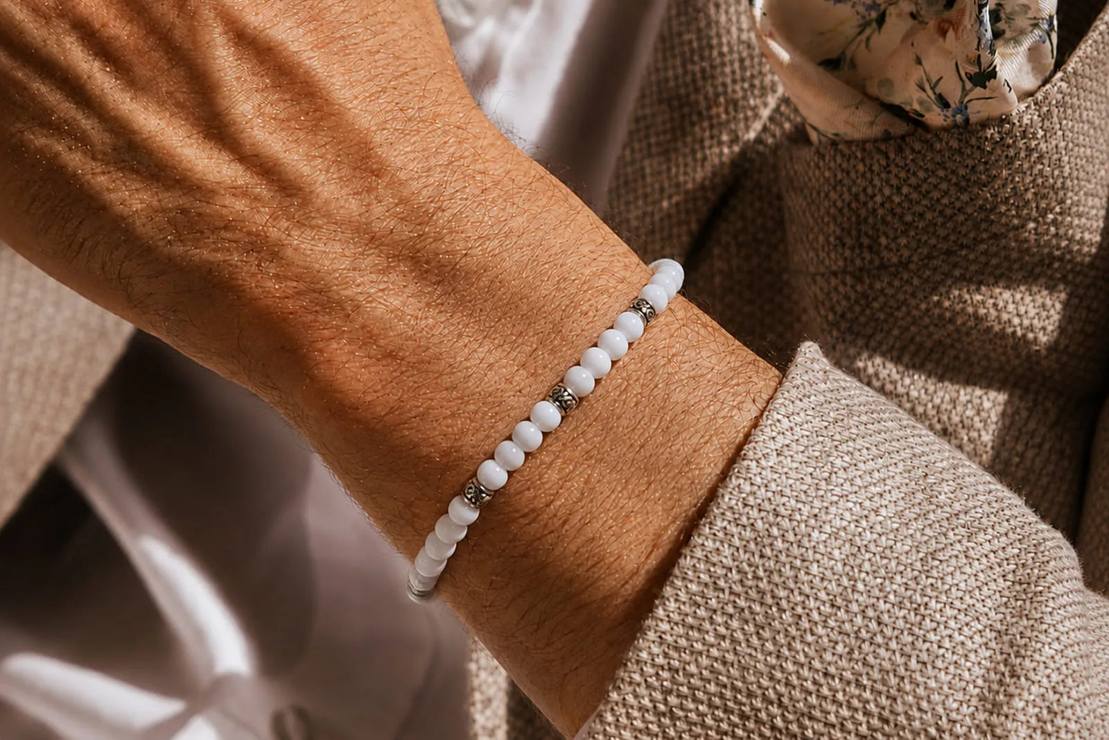 White Jade Bracelet Price shown through a slim white beaded bracelet with silver spacers, styled with a beige suit.