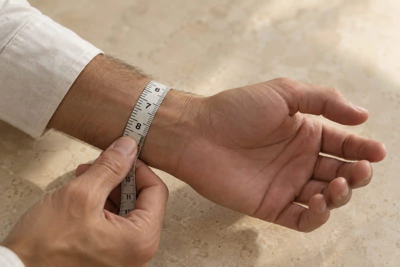 A flexible measuring tape wrapped around a man's wrist to measure its circumference for bracelet sizing.