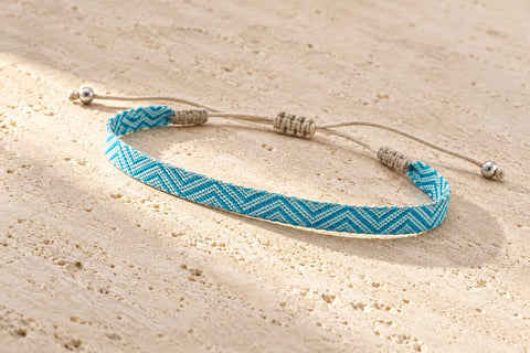 Turquoise and pale blue chevron bracelet on light stone, with beige adjustable cords and silver-tone end beads.