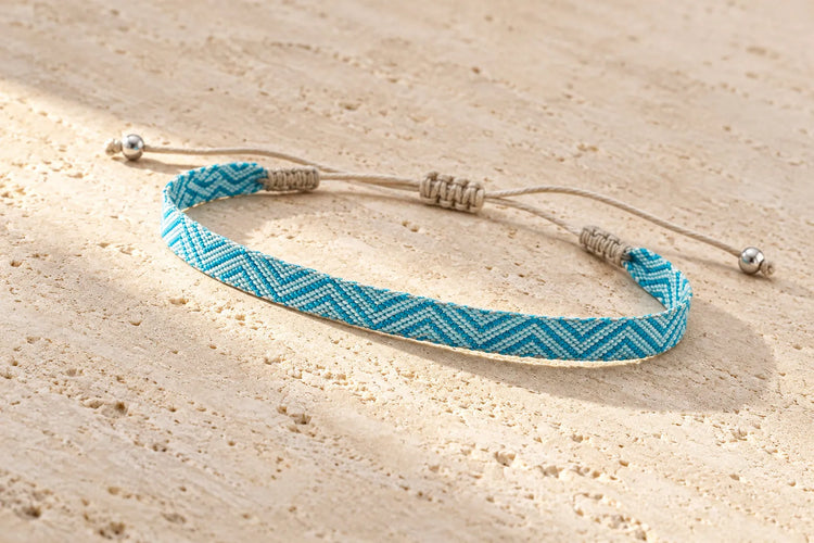 Turquoise and pale blue chevron bracelet on light stone, with beige adjustable cords and silver-tone end beads.