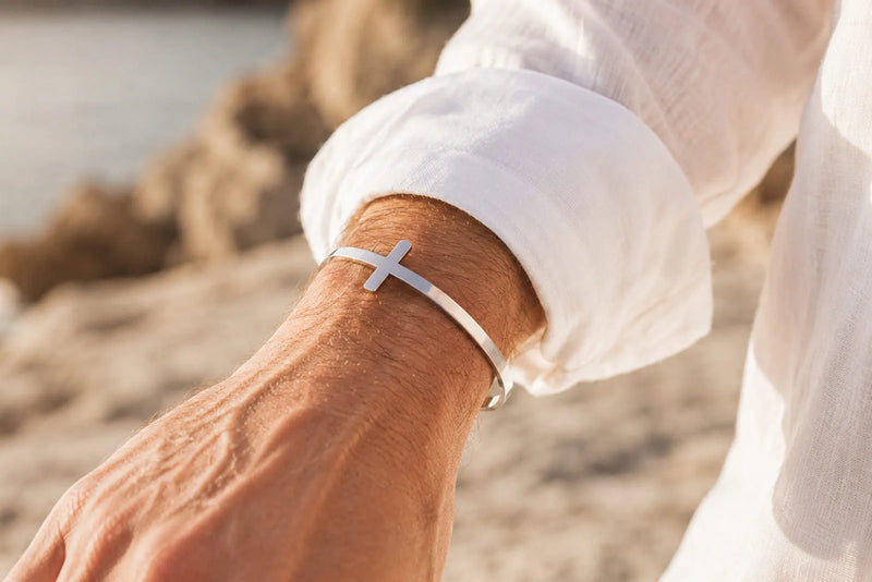 Man wearing a stainless still cross bracelet with a white linen shirt