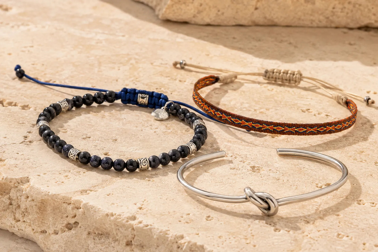 Beaded, woven and silver cuff bracelets for boyfriend arranged naturally on warm travertine stone.