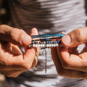 Close-up of a person holding stacked wristlets with beads and cords in blue, black, and white tones