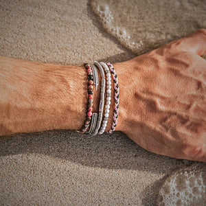 Close-up of bonded bracelets stacked on a man's wrist on sandy beach