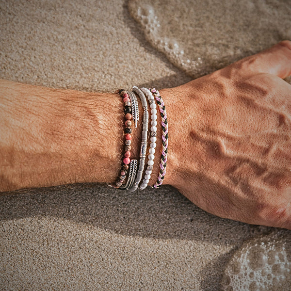 Close-up of bonded bracelets stacked on a man's wrist on sandy beach