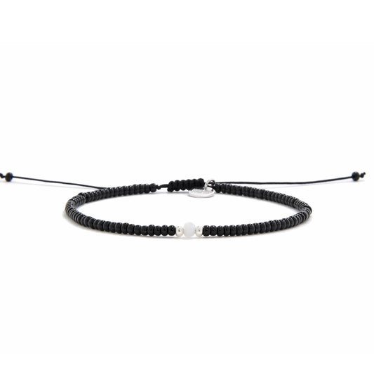 A straight-on view of an adjustable bead bracelet black with a single white bead in the center, presented on a white background.