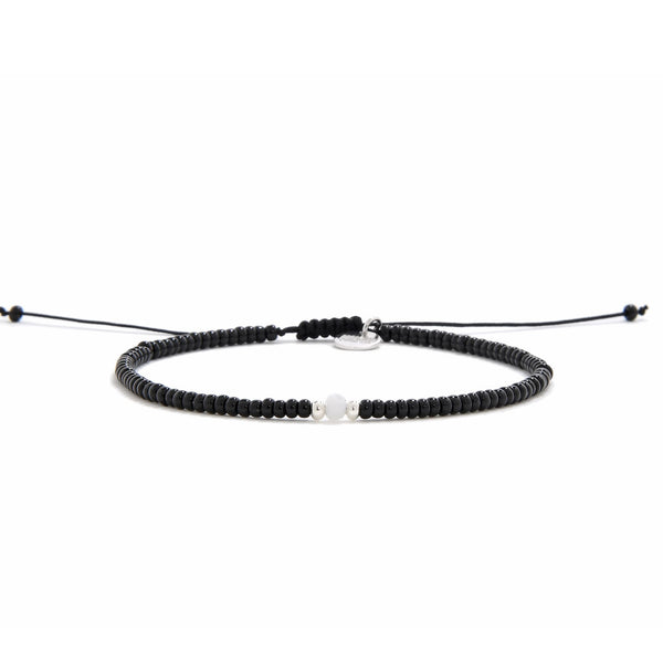 A straight-on view of an adjustable bead bracelet black with a single white bead in the center, presented on a white background.