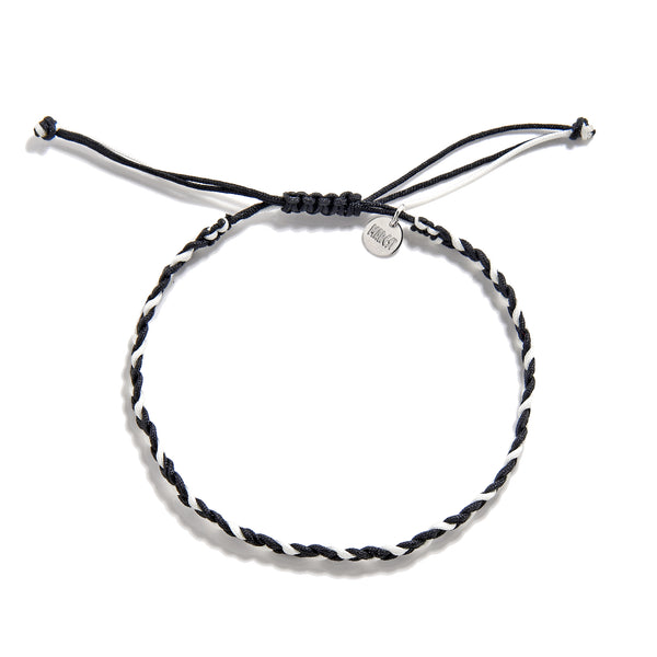 Flat lay of adjustable black and white friendship woven bracelet with charm tag and knot