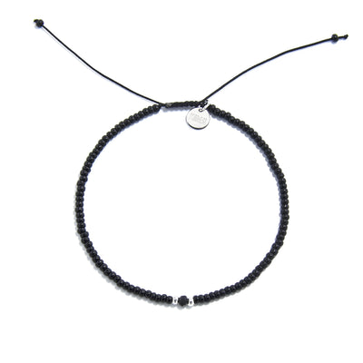 An adjustable mens beaded bracelet with black beads and a silver charm, lying flat on a white surface.