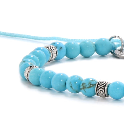 Detailed view of turquoise bracelet with smooth beads and silver accents on blue cord.