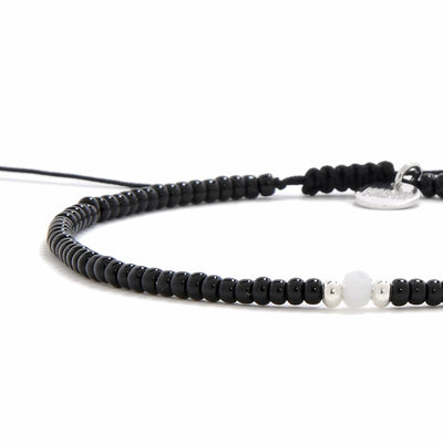 A detailed, angled view of a bead bracelet black with a matte white bead and two silver accent beads.