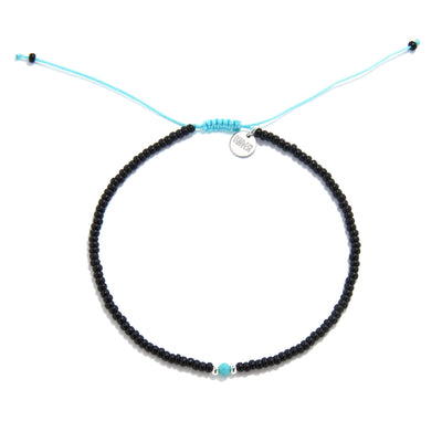 A round beaded bracelet with black beads and a striking turquoise bead in the center, shot from a top-down view on a white background.