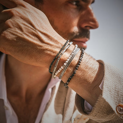 Man styling Cannes bracelet set with black and white beaded layers, silver accents, and a beige suit
