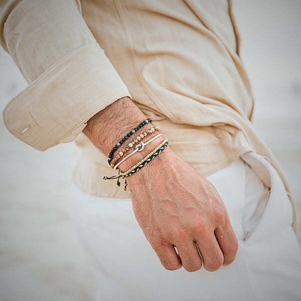Man wearing a beige shirt with stacked Capri bracelets in neutral and dark tones.