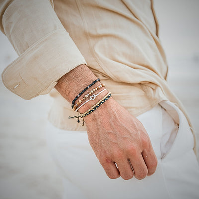 Close-up of men's wrist wearing layered beach-style bracelets in beige and navy tones
