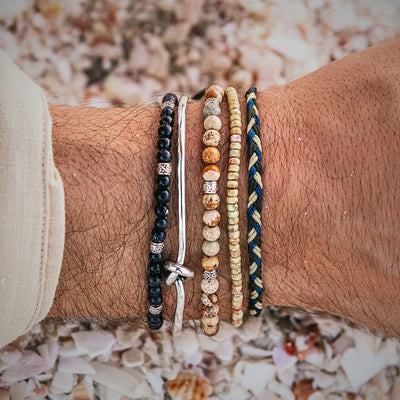 Top-down view of assorted beaded and silver bracelets worn at the beach