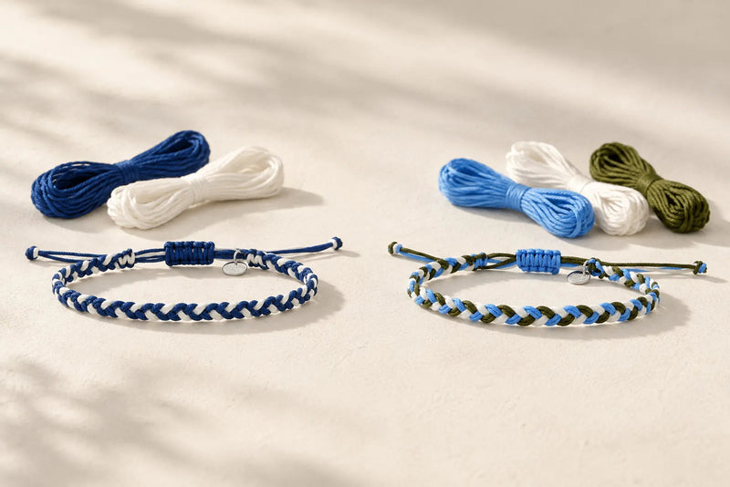 Two woven friendship bracelets made with blue, white, and olive green string, displayed beside matching embroidery floss on a neutral surface.