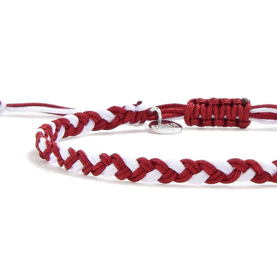 Close-up of braided red and white friendship bracelet handmade with charm tag