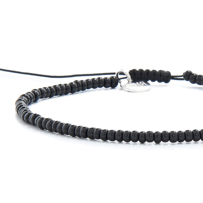 An extreme close-up of a black bead bracelet, focusing on the small, uniform beads and the engraved silver charm.
