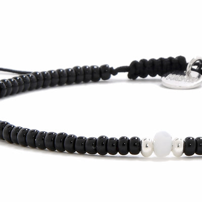 An extreme close-up of a bead bracelet black, highlighting the smooth white bead and two small silver beads in the center.