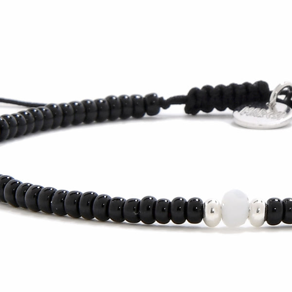 An extreme close-up of a bead bracelet black, highlighting the smooth white bead and two small silver beads in the center.