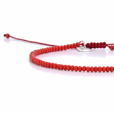 A detailed close-up of a red men beaded bracelet, showing the adjustable cord, silver charm, and small red beads.