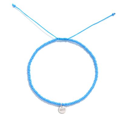 Flat lay of blue Corte beaded cross bracelet with minimalist cord and silver charm

