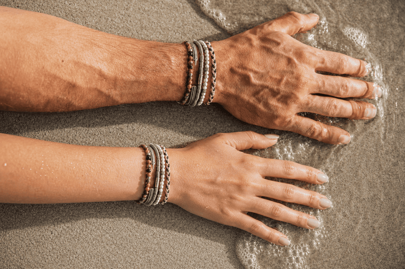 Boyfriend and girlfriend wearing matching bracelets while relaxing on the beach, showcasing coordinated bracelet styles.