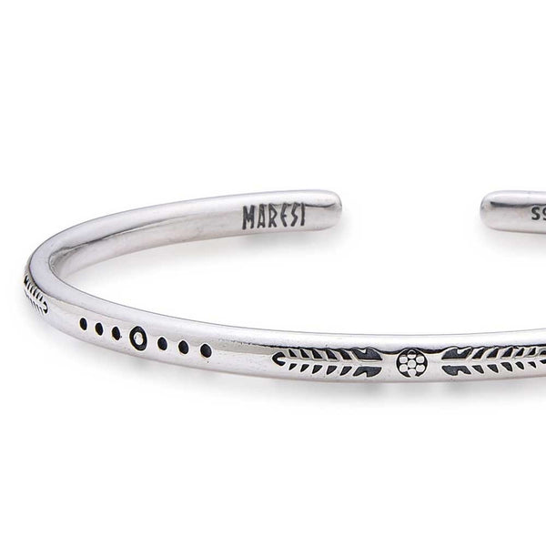 Close-up of silver bracelet bangle showing arrows and dot engravings.